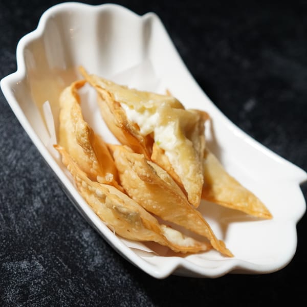 Crispy golden-brown crab rangoons with creamy filling, served in a white scalloped dish.
