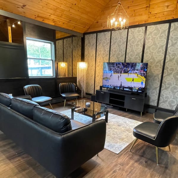 A lounge area with black leather seating, a TV showing basketball, and decorative lighting.