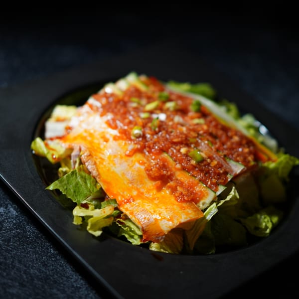 Asian-fusion dish with sliced meat, red sauce, and green onions on a bed of lettuce.