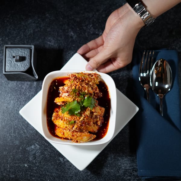 A hand places a white bowl of Eastern Pavilion's spicy Asian-fusion chicken with cilantro on a dark table.