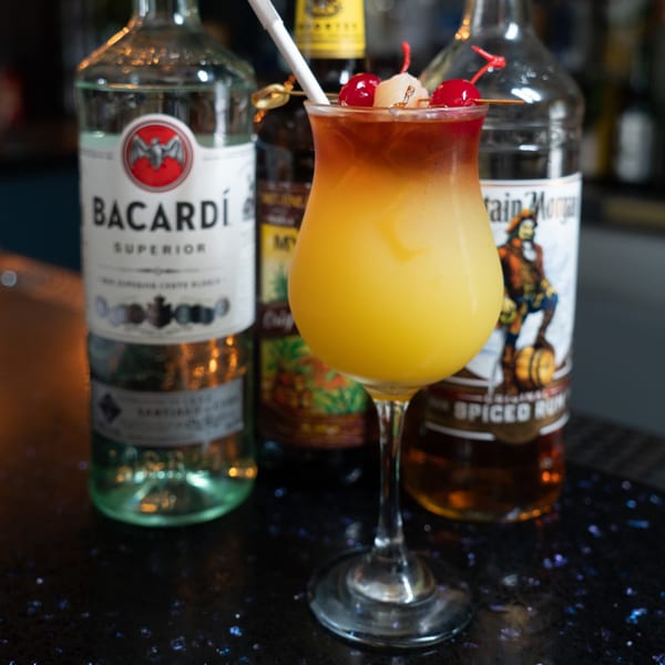 Tropical cocktail with cherries and lychee, with Bacardi and Captain Morgan bottles in the background.