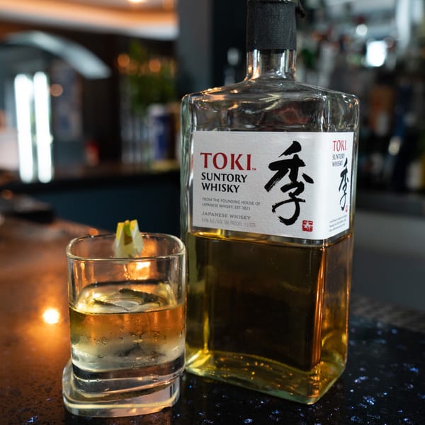 Toki Suntory Japanese Whisky bottle and a glass with ice and a lemon wedge on a bar.